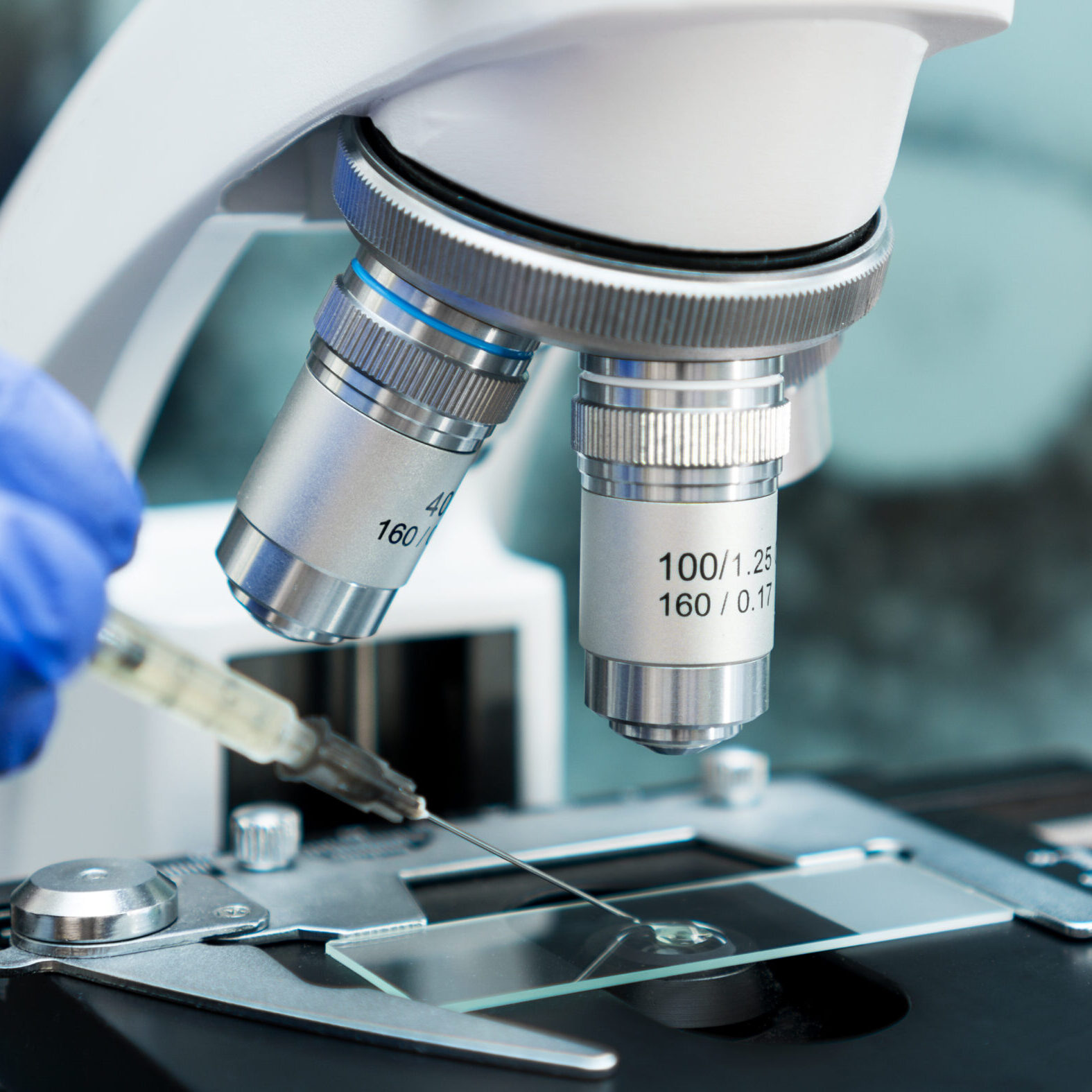 Virologist's hand in glove testing coronavirus vaccine under microscope.